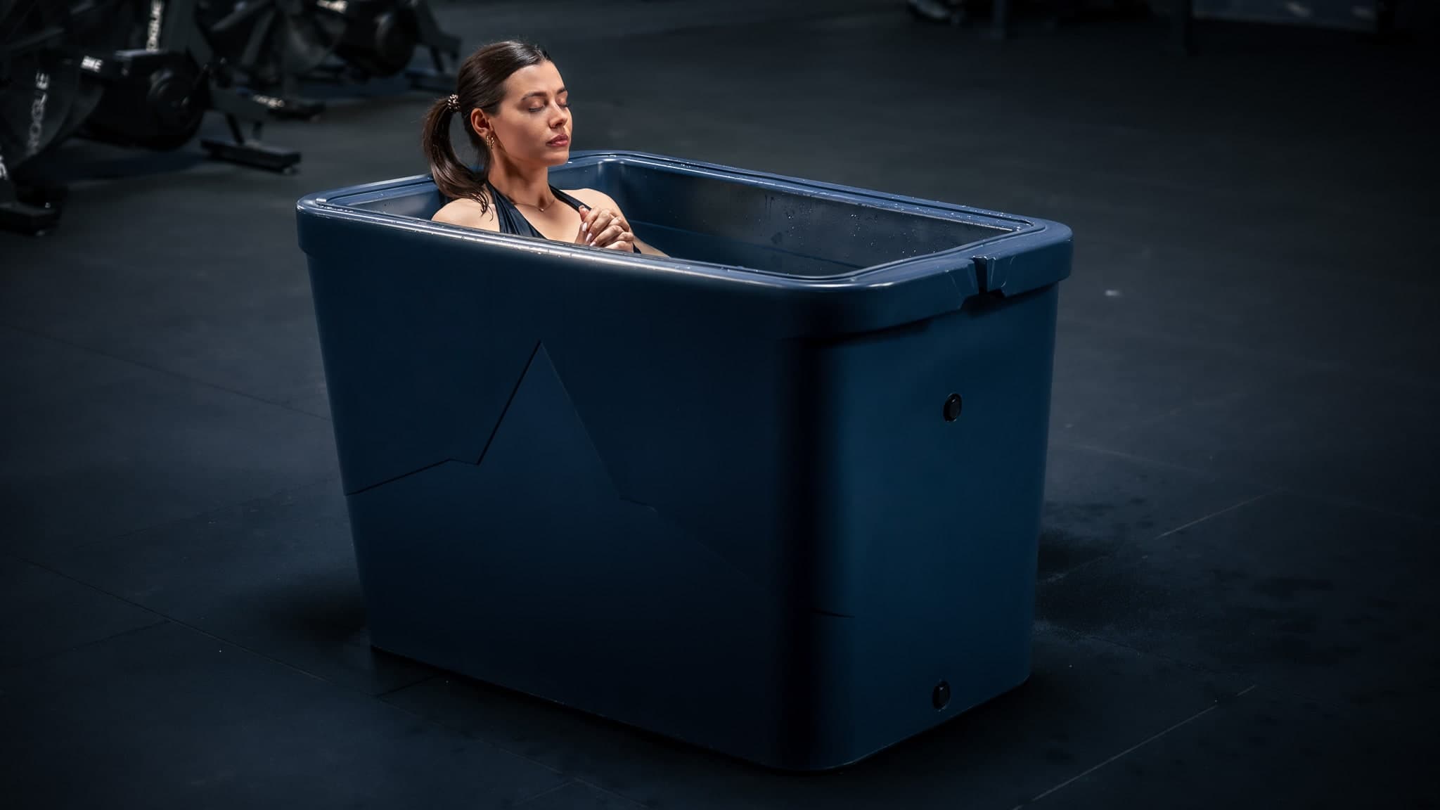 A woman sitting calm and composed in a Theralpine ice bath, eyes closed, focused.
